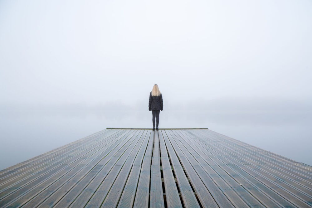 Young woman standing alone on edge of footbridge and staring at lake.