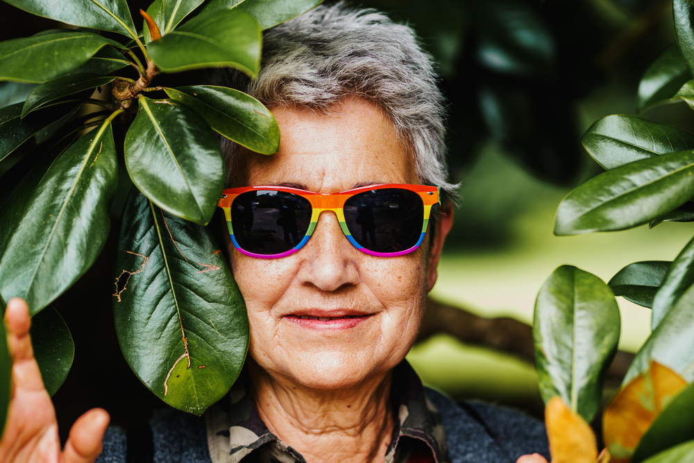 horizontal portrait of older lady from the lgbt community smiling with sunglasses among green plants.