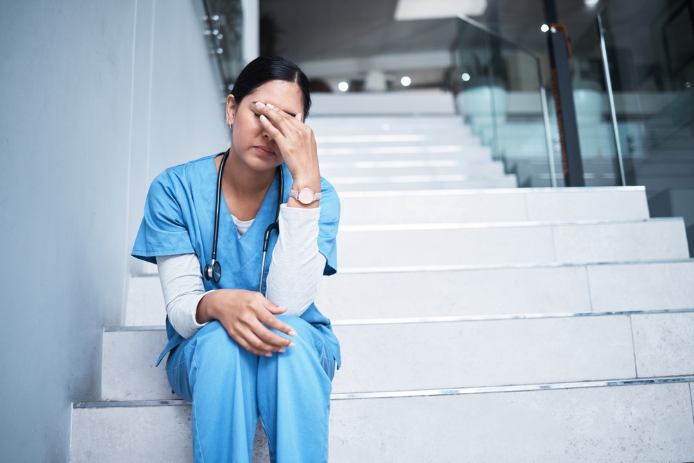 Shot of a doctor looking stressed while sitting on a staircase.