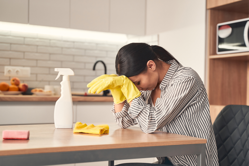 Young female person bowing her head while being tired after cleaning her apartment