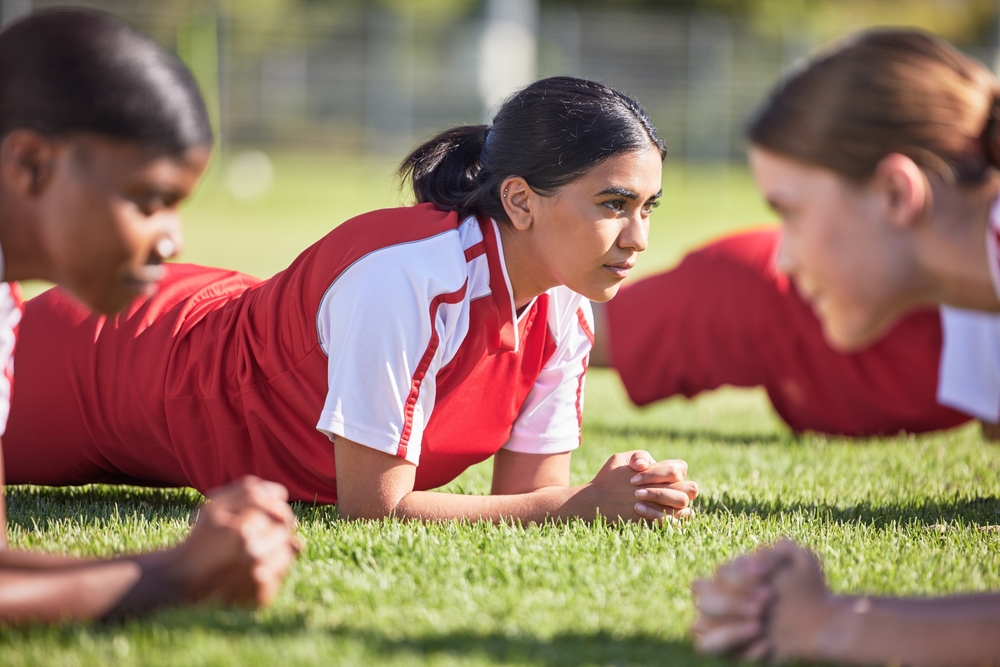 Women soccer players in a team doing the plank fitness exercise in training together on a practice sports field.