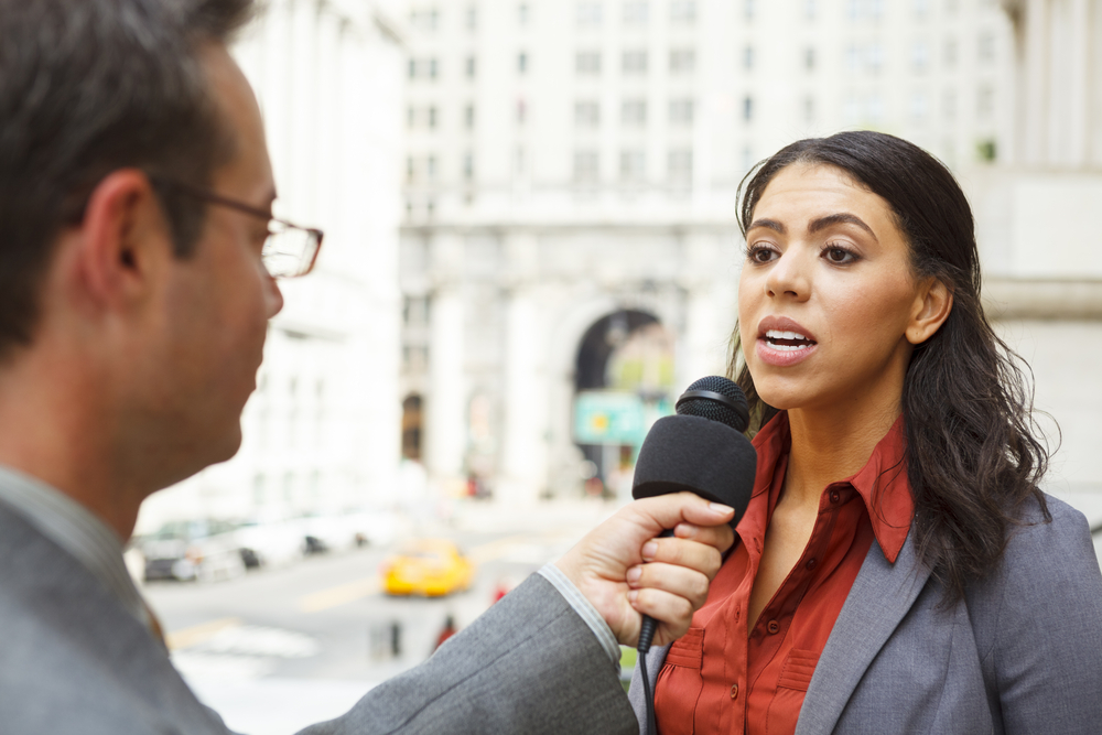 A man with a microphone interviewing a professionally dressed woman in the city.