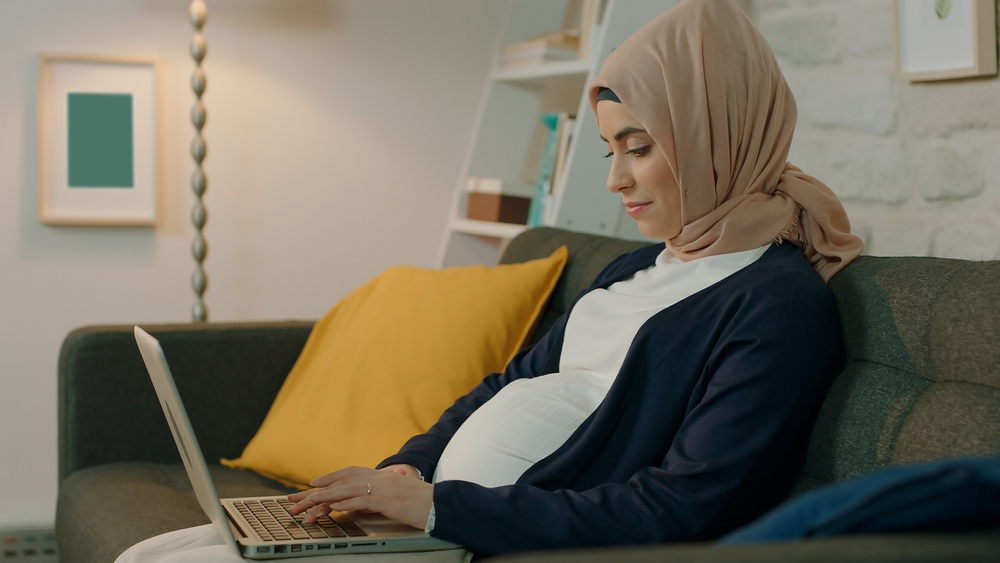 Pregnant young woman doing computer work in indoor room with lights.