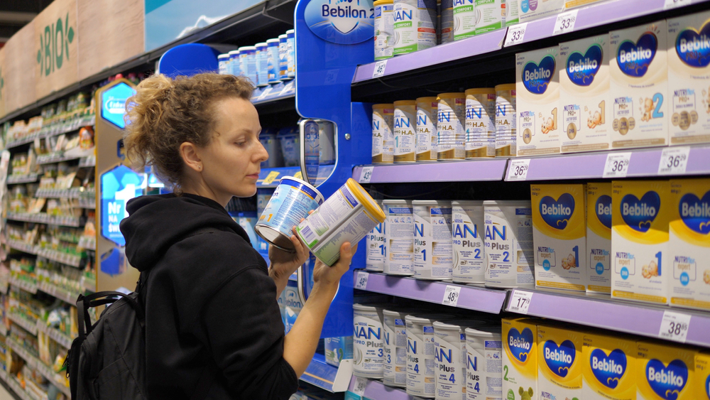 Young mother choosing baby formula for her newborn. Picking different options from the shelf and reading the labels.
