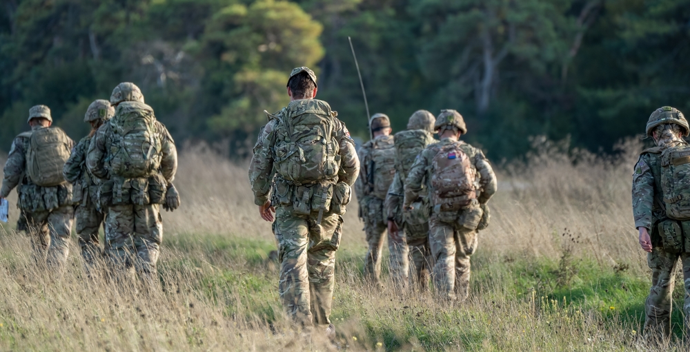 8 male and female British army soldiers tabbing with 25Kg bergens across open countryside, Wiltshire UK