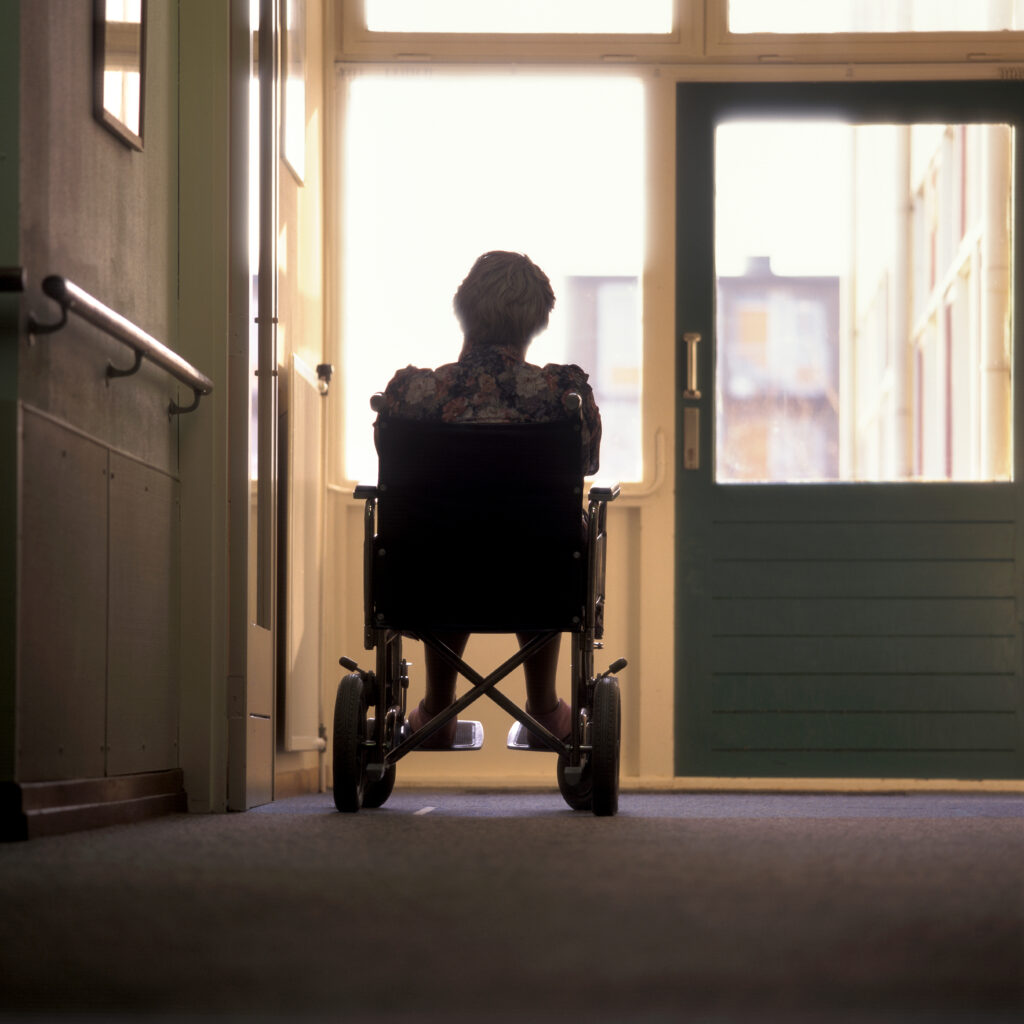Back view of a female senior in a wheelchair in a nursing home looking outside